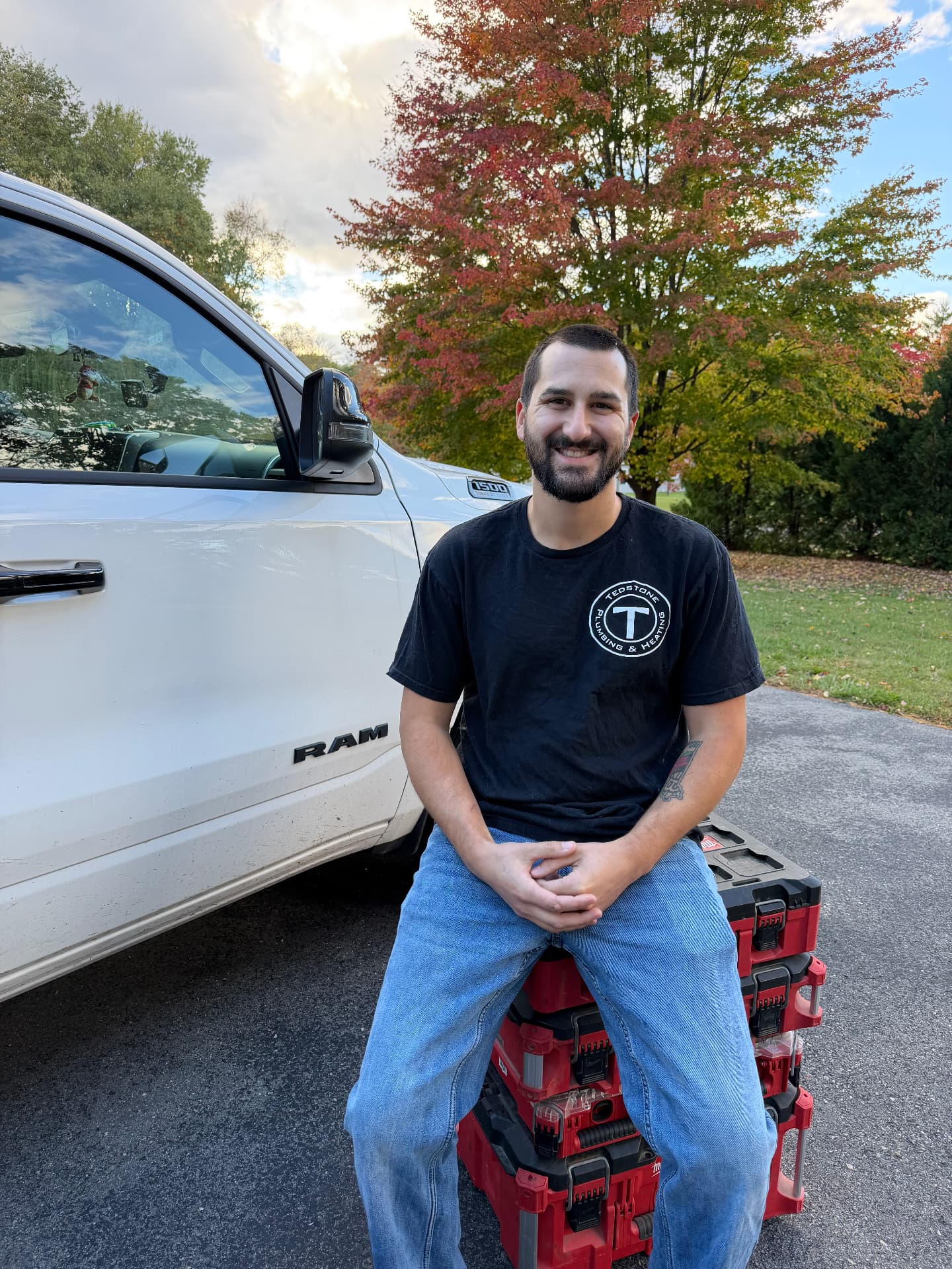 Adam Tedstone, owner and licensed master plumber at Tedstone Plumbing & Heating LLC, seated on a stack of toolboxes beside his work truck