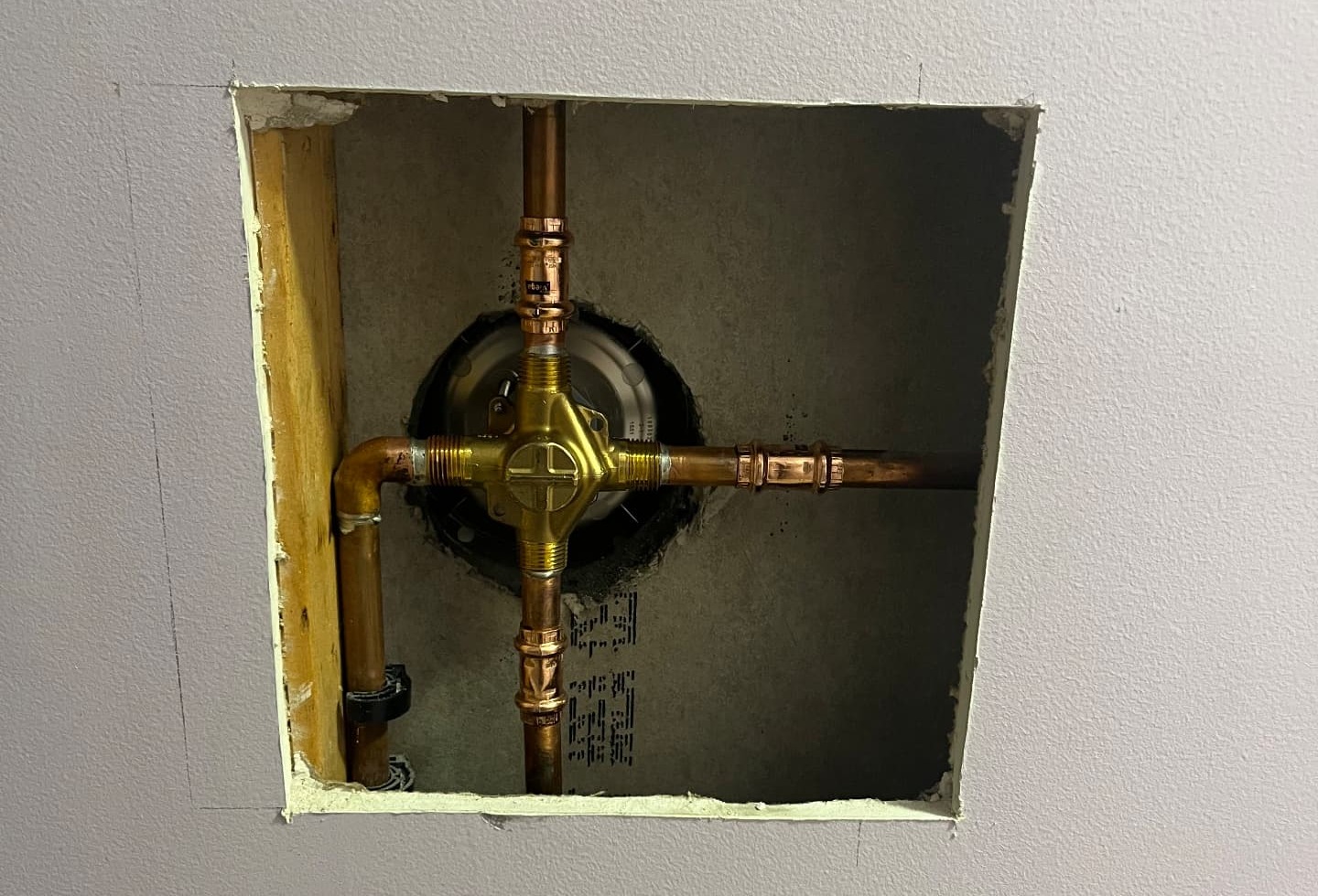 Brass shower valve with copper supply lines and pressed fittings set inside an open wall cavity, before the handle and trim plate are installed