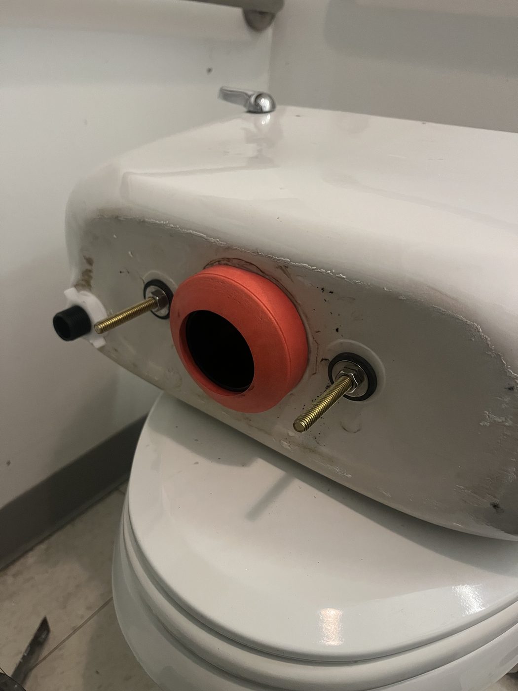 Toilet tank removed from the bowl showing the tank bolts and rubber gasket during a rebuild