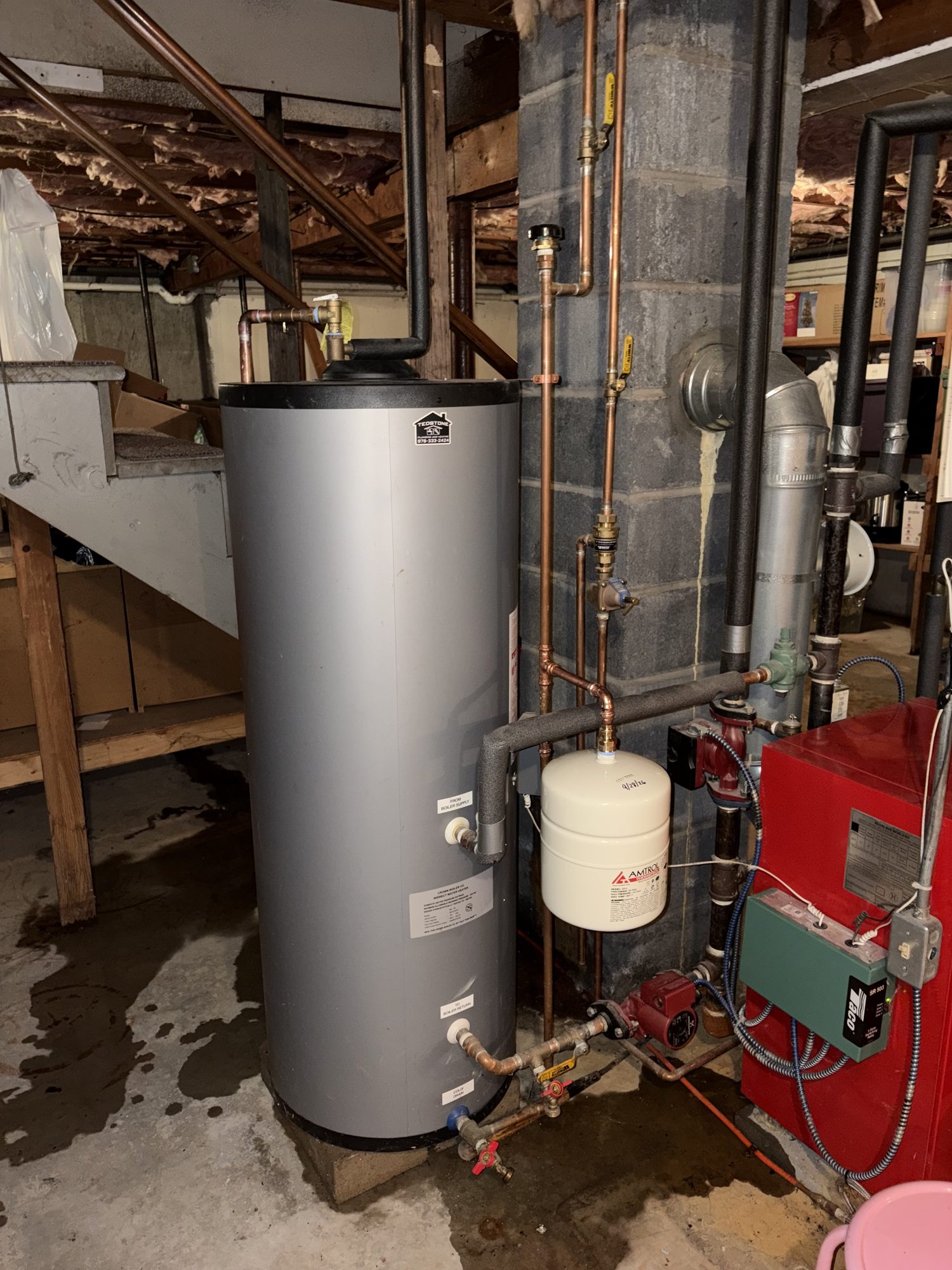 Gray indirect water heater tank beside a boiler with copper piping in a Lancaster, MA basement
